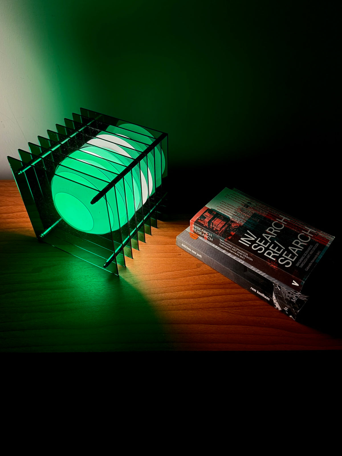 A layered green acrylic lamp glowing beside a stack of books.