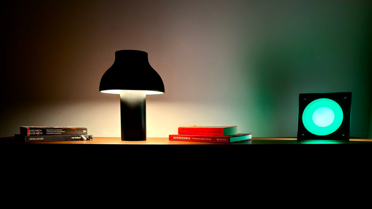 Two lamps lit on a walnut sideboard in a dim room, one casting green light and one warm white across the wall.