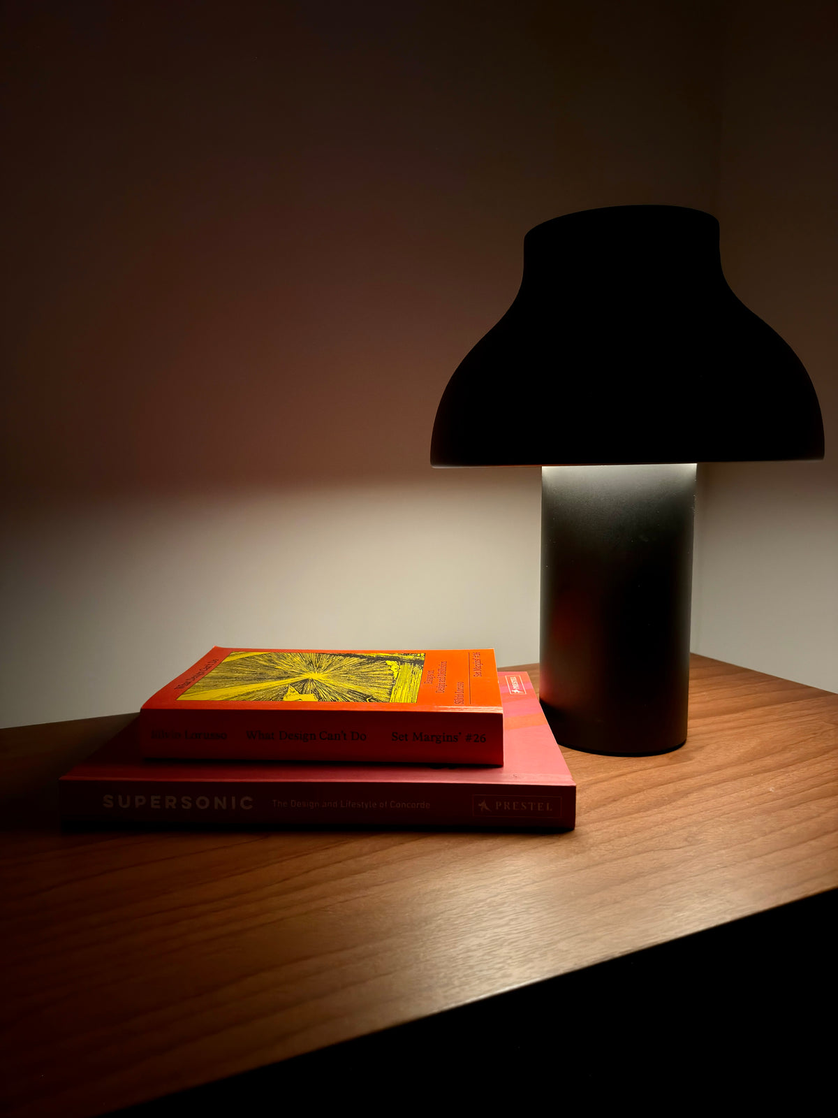 A black mushroom-shaped table lamp lit on a walnut sideboard beside a stack of books.